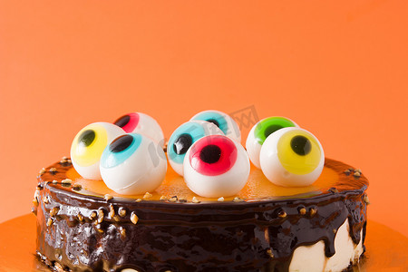 橙色背景中突显的带有糖果眼装饰的万圣节蛋糕