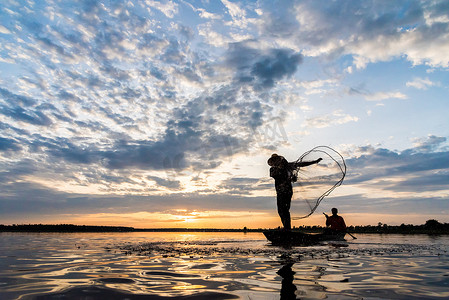 蓝色湖水摄影照片_渔民在 W 日落时撒网捕鱼的剪影