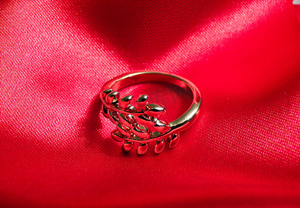 红色绸布摄影照片_红色丝绸布上的金戒指。