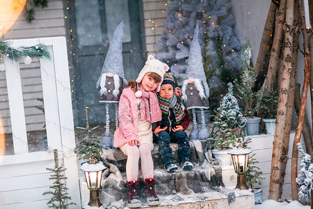 快乐的小孩坐在户外圣诞装饰屋的门廊上