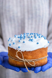 戴着蓝色手套的手拿着带有白色浇头和蓝色洒水的复活节蛋糕。