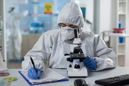 穿着防护服的生物学家研究员使用医学显微镜分析化学品