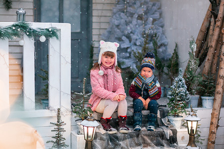 小孩圣诞老人摄影照片_快乐的小孩坐在户外圣诞装饰屋的门廊上