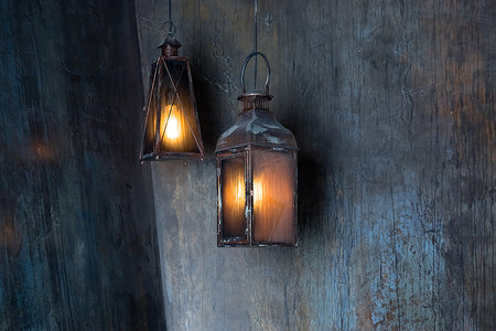 挂着的灯笼摄影照片_夜里，灯笼挂在屋前。挂着黑色的铁灯笼，在黑夜里燃烧着肮脏的玻璃。装饰和室内概念