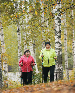 在斯堪的纳维亚散步期间，穿着羽绒服的成熟女性在秋季公园爬山