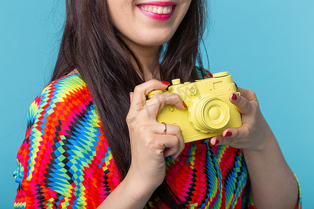 女人的特写镜头手里拿着一个摆在蓝色背景上的黄色老式相机模型。