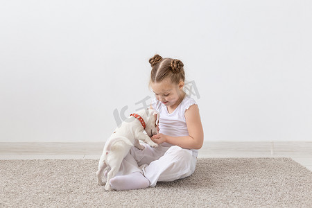 宠物家摄影照片_宠物主人、孩子和狗的概念 — 小女孩和可爱的杰克罗素梗小狗坐在地板上玩耍