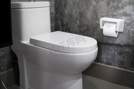 家庭浴室白色马桶上的白色悬挂式马桶座，墙上铺着混凝土风格的灰色瓷砖和卫生纸。