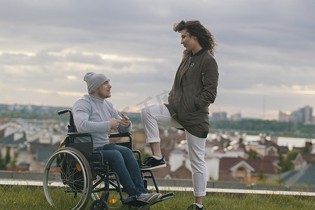 关爱残疾人关爱摄影照片_美丽的女人和年轻的残疾人在山上俯瞰城市