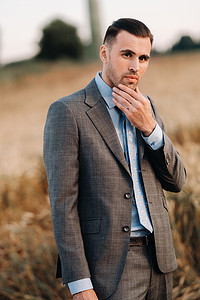 西装和领带摄影照片_麦田里一个穿着灰色西装的商人的画像。一个穿着夹克和领带的自然界男人