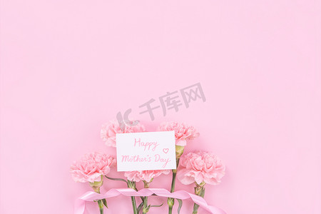 清新明亮的背景摄影照片_美丽、清新优雅的康乃馨花束与白色问候感谢礼品卡隔离在明亮的粉红色背景、顶视图、平躺概念。