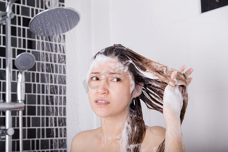 不快乐的女人用洗发水和淋浴洗头