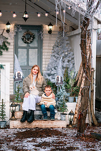 小孩圣诞老人摄影照片_快乐的小孩坐在户外圣诞装饰屋的门廊上