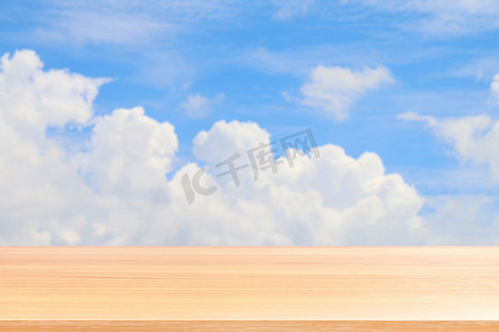 空木桌地板在模糊的蓝天和云背景，木桌板空的前面模糊天蓝色，木板空白在天空与透视棕色木桌模拟展示产品