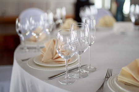 桌上的餐具，透明玻璃香槟杯，白色餐具盘，米色桃色餐巾，刀叉，没有人的桌子，没有食物的干净餐具