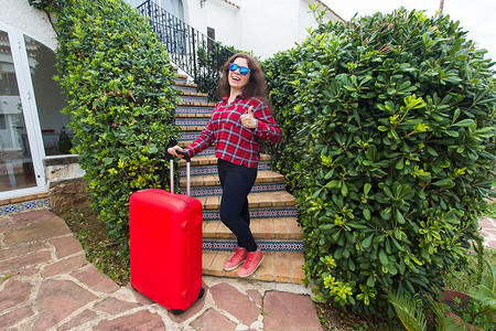 旅行、旅游和旅行概念 — 带着红色旅行箱的年轻女性竖起大拇指