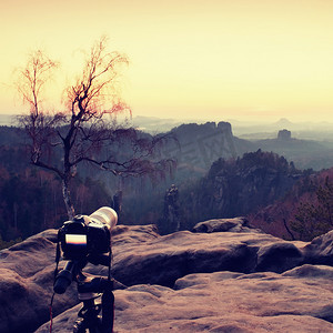 站在山峰上摄影照片_日落后，带大相机的三脚架站在山峰上。