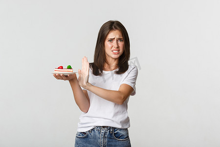 微信表情包嗯嗯摄影照片_厌恶的年轻女子拒绝吃难吃的蛋糕，做出拒绝的手势，并做出痛苦的表情