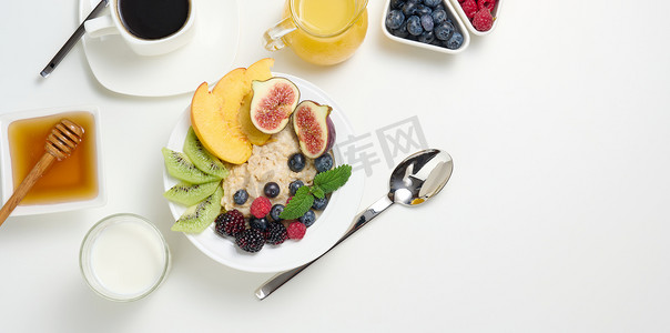 一杯黑咖啡、一盘燕麦片和水果、蜂蜜和白桌上的一杯牛奶，一顿健康的早餐，俯视