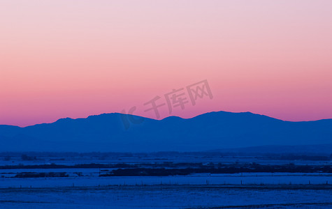 美国蒙大拿州加拉廷县博兹曼北部冬季日落后的积雪覆盖的田野和遥远的博尔德山脉