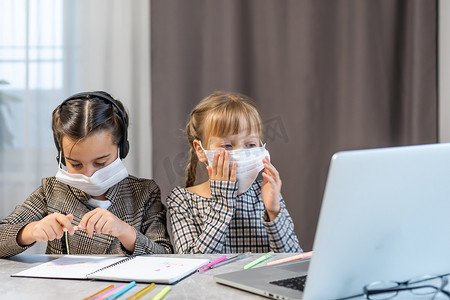 病毒大流行期间的家庭教育学习 — 两个孩子在客厅里画画，戴着外科口罩以保护他们免受病毒侵害。