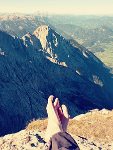 站在山峰上摄影照片_穿着深色远足裤的裸男汗腿在春谷上方的山峰上休息。