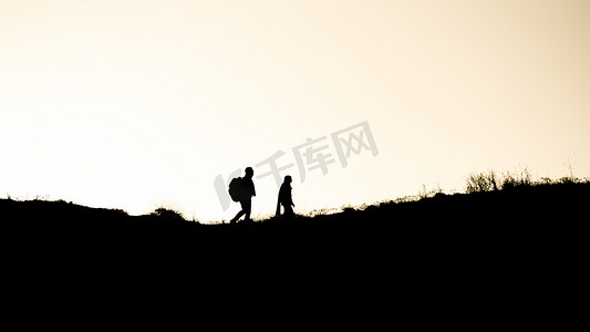 一对夫妇在日落时分在山上散步的剪影。