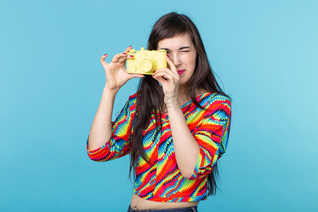 微笑的年轻女子手里拿着一个摆在蓝色背景上的黄色老式相机模型。