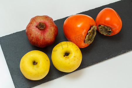 黑石板上的苹果、石榴和成熟的柿子果实。