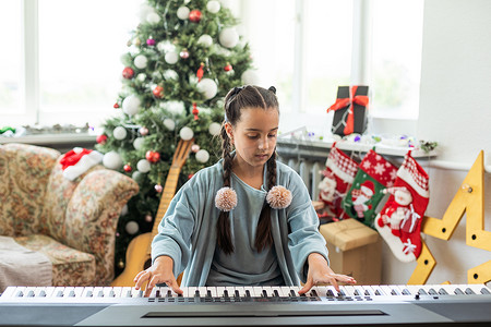 可爱的小女孩除夕夜在圣诞树的背景下弹钢琴
