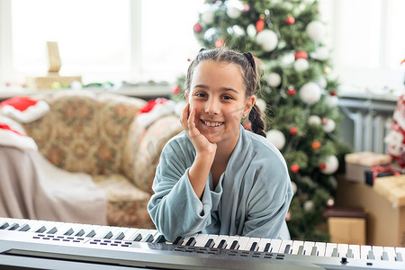 可爱的小女孩除夕夜在圣诞树的背景下弹钢琴