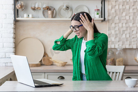 迷茫的摄影照片_在家厨房用笔记本电脑工作的女性压力很大，在网上​​得到了坏消息