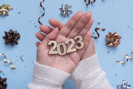数字倒计时创意摄影照片_2023 年新年的数字，在明亮的节日背景下，女性手中有弓和珠的顶视图