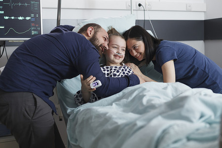 在儿科医院病房里，快乐的年轻父母拥抱生病住院康复的小女孩。