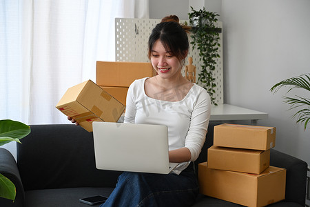 微笑的年轻女性在线卖家在笔记本电脑上检查产品采购订单。