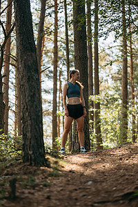 身着运动服的年轻女跑步者站在绿色森林的小路上，准备在准备马拉松时跑步