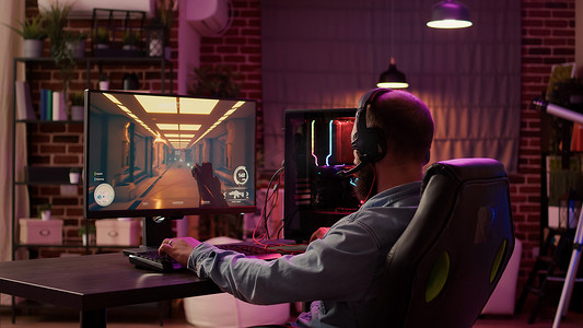 使用电脑游戏设置的男子放松地玩多人在线动作游戏，在耳机上与团队交谈