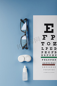 镜片摄影照片_眼科配件眼镜和镜片，带有用于蓝色背景视力矫正的视力测试图