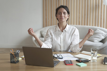 有魅力的女性企业家闭着眼睛坐在笔记本电脑前的办公桌上，以轻松的姿势