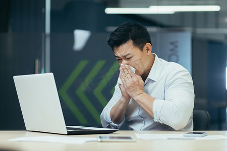 办公室里的病人咳嗽、流鼻涕，亚洲商人感冒了，在办公室用笔记本电脑工作