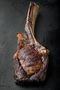 多汁的牛排在骨战斧大理石牛肉上烤，黑色石头背景