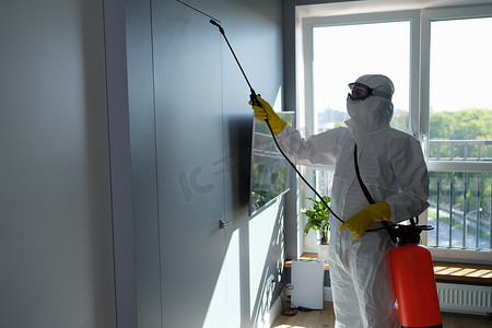 身穿防护服和面罩的工人在室内喷洒化学品