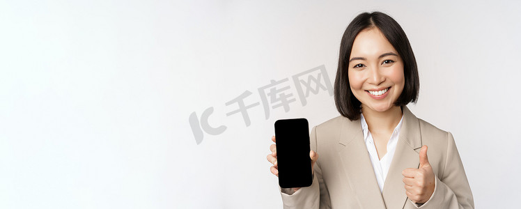 手机批准摄影照片_微笑的亚洲女人展示智能手机屏幕和竖起大拇指。