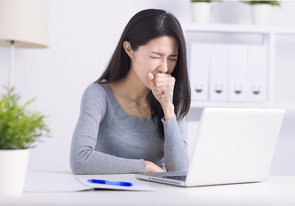 生病的年轻女性忙于笔记本电脑咳嗽，在工作场所与冠状病毒或流感作斗争