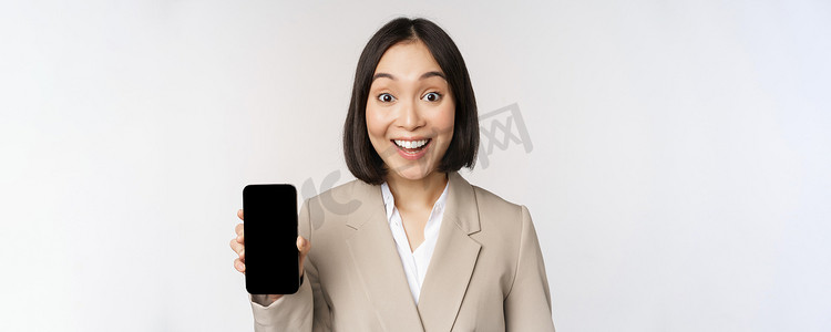 亚洲企业女性展示应用程序界面、手机屏幕、做出惊讶的表情、哇，站在白色背景上