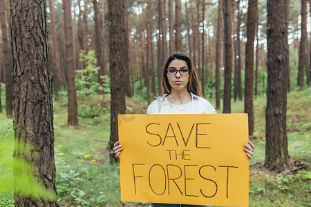 保护环境海报摄影照片_年轻女子在树林纠察队做志愿者，举着拯救森林的海报
