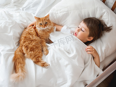 躺在床上摄影照片_幼儿和可爱的姜猫躺在床上。