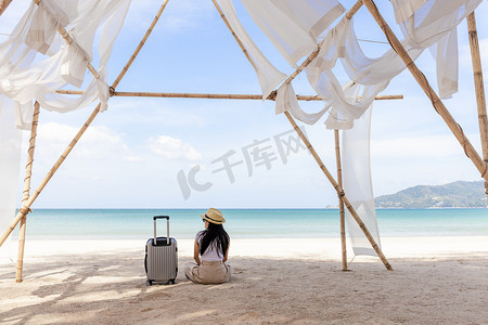 夏天，年轻快乐的女人带着旅行箱坐在海滩上。