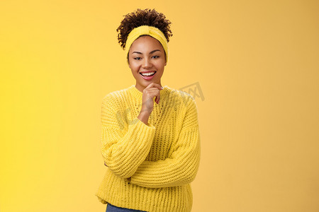 感兴趣兴奋热情好看的女企业家时尚毛衣头带爆炸头发型触摸下巴深思熟虑的微笑喜欢项目想法站在黄色背景感兴趣