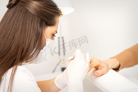 药健康摄影照片_戴防护面罩和白手套的美甲大师在女性指甲上涂上抛光剂。